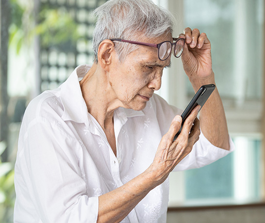 Senior holding glasses on his forehead and looking at his smartphone