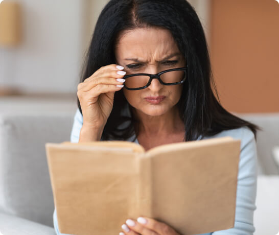 Woman holding glasses while reading a book